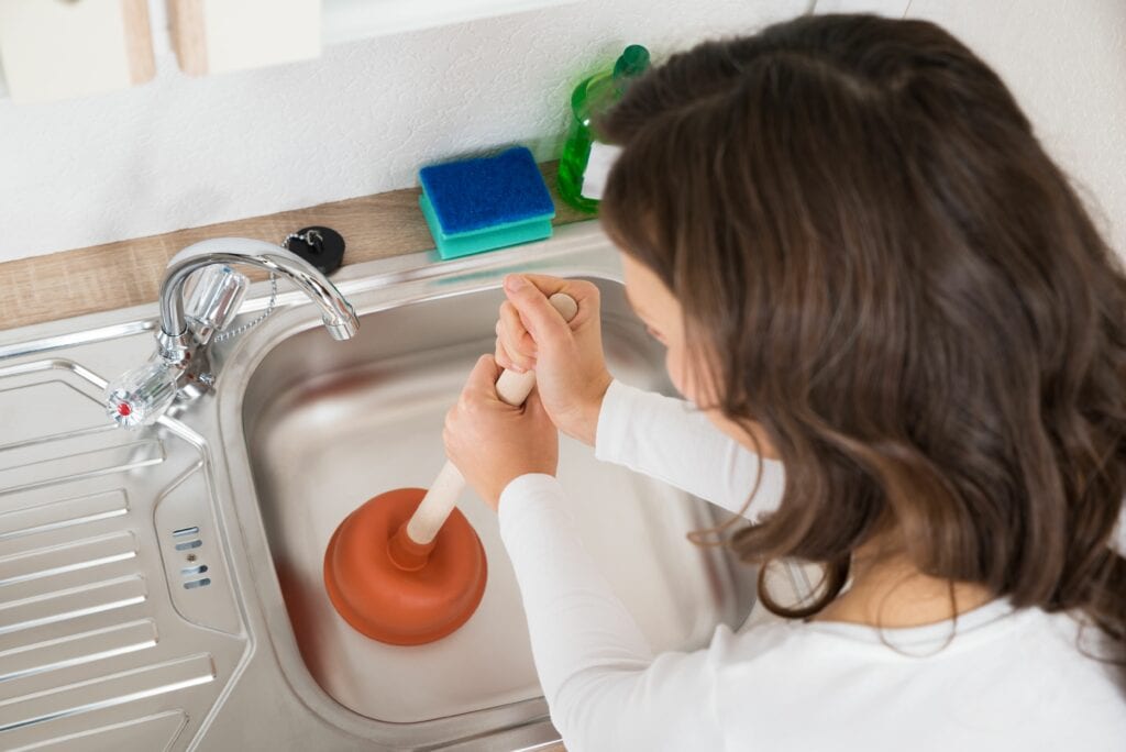 Image of someone using a plunger on their clogged sink. How Can I Avoid a Plumbing Emergency?